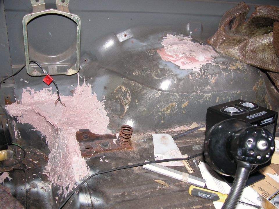 Stripped vehicle interior with pink body filler on floor and wheel well, tools and work lamp nearby