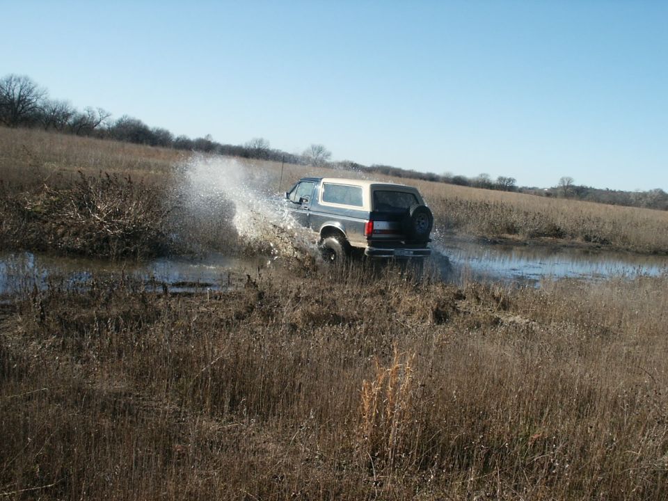 Dark Ford Bronco with white top splashing through standing water in a winter field