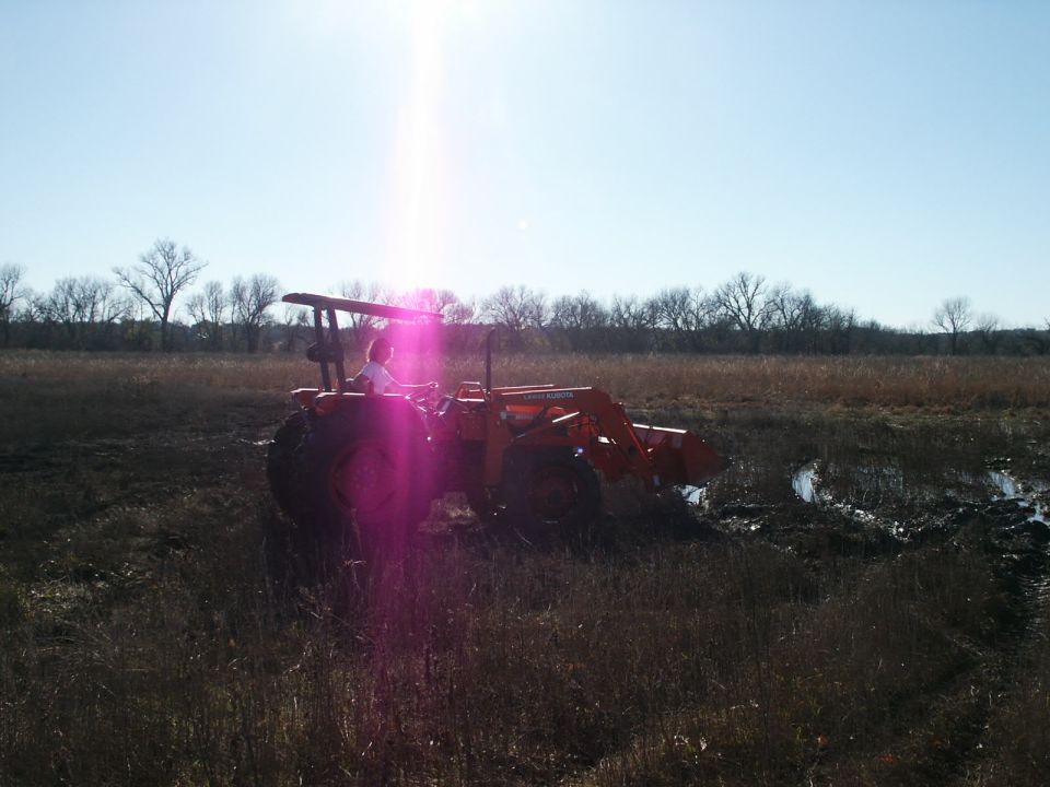 Orange tractor with front loader in a muddy field