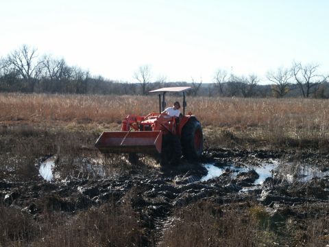 1991 Ford Bronco - A person drives a tractor through a muddy, watery field under a clear sky.