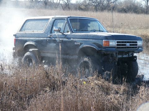 1991 Ford Bronco - This 1991 Ford Bronco navigates a muddy terrain, kicking up water and grass.