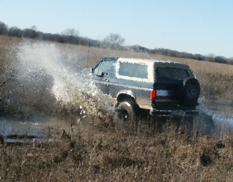 1991 Ford Bronco - A 1991 Ford Bronco kicks up a large spray as it drives through a muddy, watery field.