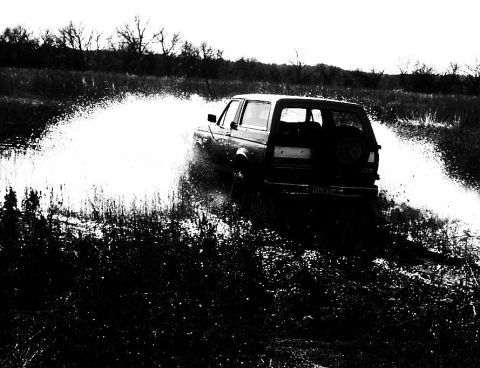 1991 Ford Bronco - Ford Bronco driving through a wet, grassy field, spraying water.