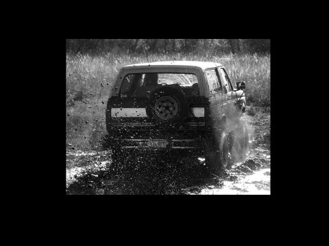 1991 Ford Bronco - A 1991 Ford Bronco navigates a muddy terrain, kicking up water as it drives through the mire.