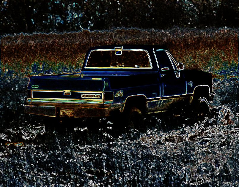 Dark blue pickup truck, likely 1980s Chevrolet C/K series, parked in tall grass