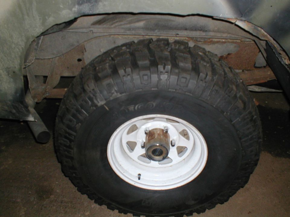 Mud-terrain tire on white steel wheel in a rusted-out Bronco wheel well