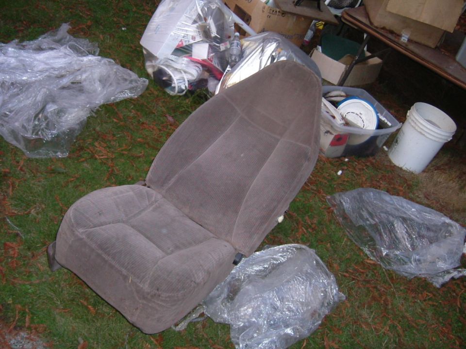 Grey cloth bucket seat removed from a truck sitting on grass beside plastic sheeting and boxes