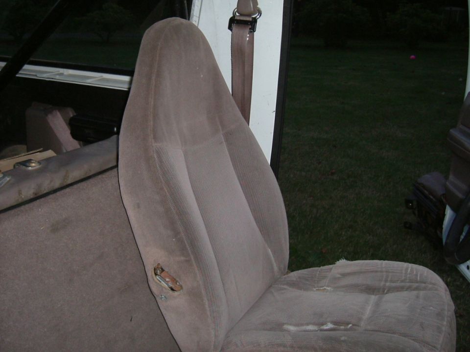 Front seat and part of rear seat in a vehicle. Seat fabric is worn and torn in places