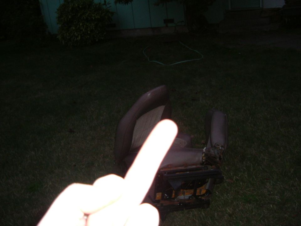 Brown vinyl and cloth bucket seat set on a lawn at night, rails exposed