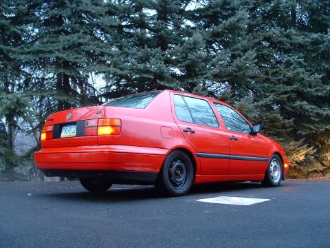 1994 Volkswagen Jetta - A red sedan is viewed from its rear three-quarter angle, parked outdoors.
