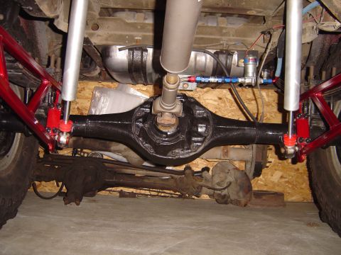1978 Ford Bronco - Underside view of a vehicle's rear axle and suspension system, showing custom red framing and silver shock absorbers.
