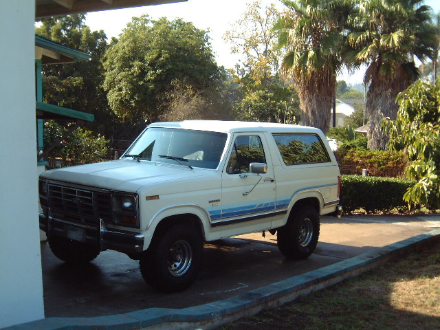 White Ford Bronco with blue stripes parked in a driveway, front three-quarter view
