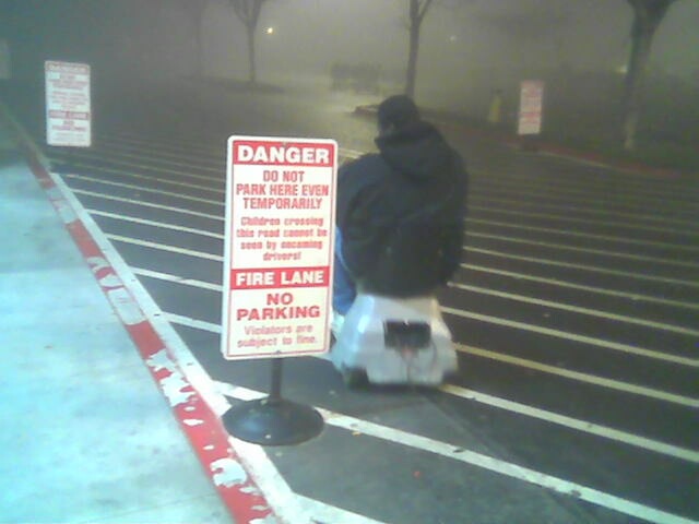 Person on motorized scooter near a 'Danger Do Not Park Here' sign in a foggy parking lot