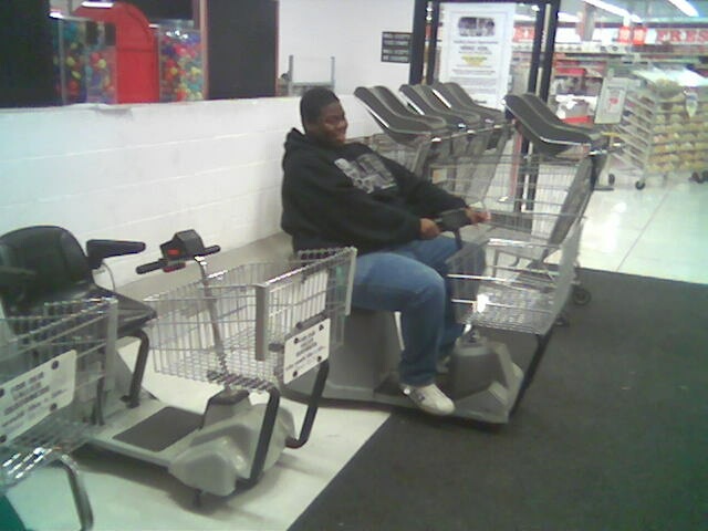 Guy riding a mobility scooter in a store aisle, next to shopping carts