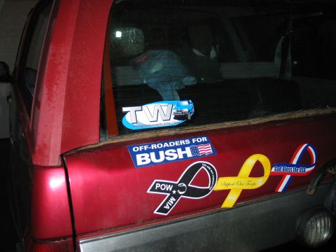 1995 Ford Bronco - The rear of a red SUV is covered in stickers, including political and support ribbons.