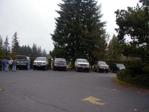 1994 Ford Explorer - Multiple SUVs are parked in a lot with trees in the background under an overcast sky.