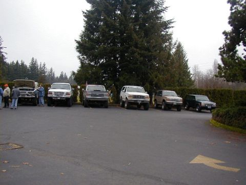 1994 Ford Explorer - A group of SUVs and trucks, including a white 1994 Ford Explorer, are parked in a lot on an overcast day.
