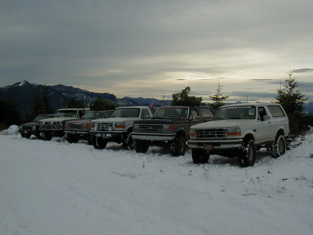 Row of lifted Ford Broncos parked in snow at a mountain overlook at dusk