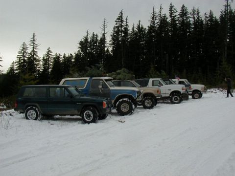 1994 Ford Explorer - A group of off-road vehicles are parked in a snowy area, with a line of trees in the background.