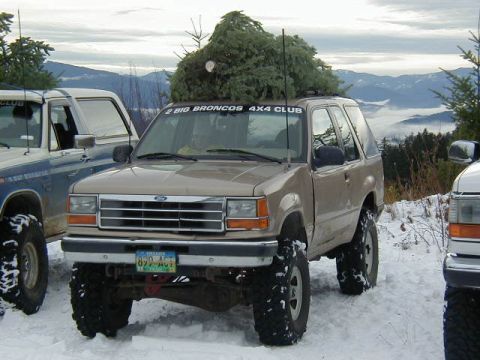 1994 Ford Explorer - A tan 1994 Ford Explorer, equipped with off-road tires, transports a Christmas tree through a snowy landscape.