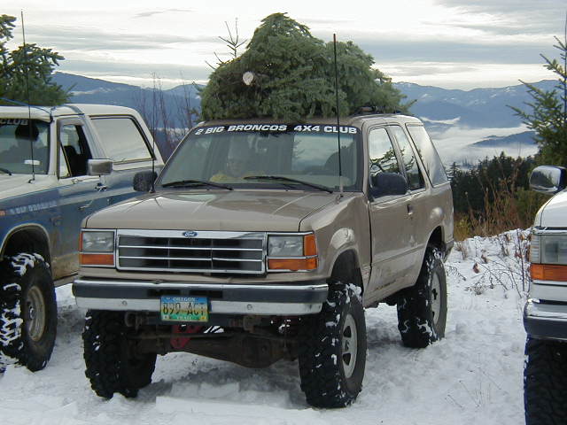 Lifted tan Ford Explorer in snow with Christmas tree on roof and 4x4 club windshield banner