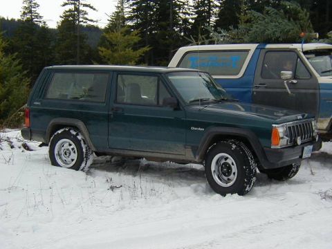 1994 Ford Explorer - A green Jeep Cherokee is parked in the snow next to a blue Ford Bronco loaded with Christmas trees.