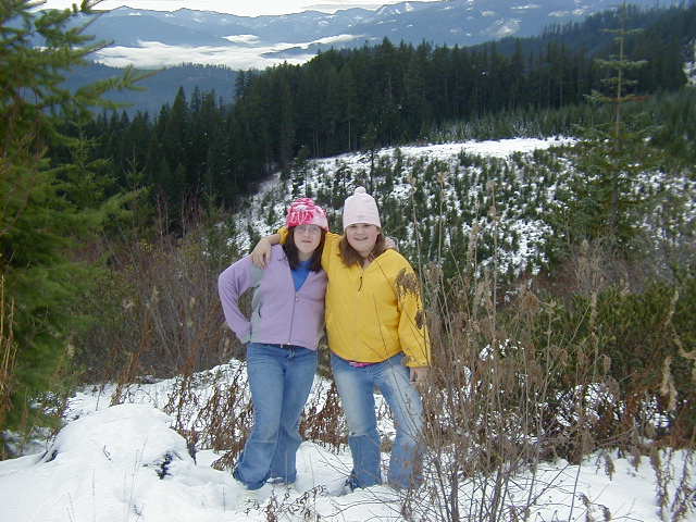 Two people in winter clothes posing on a snowy forested hillside