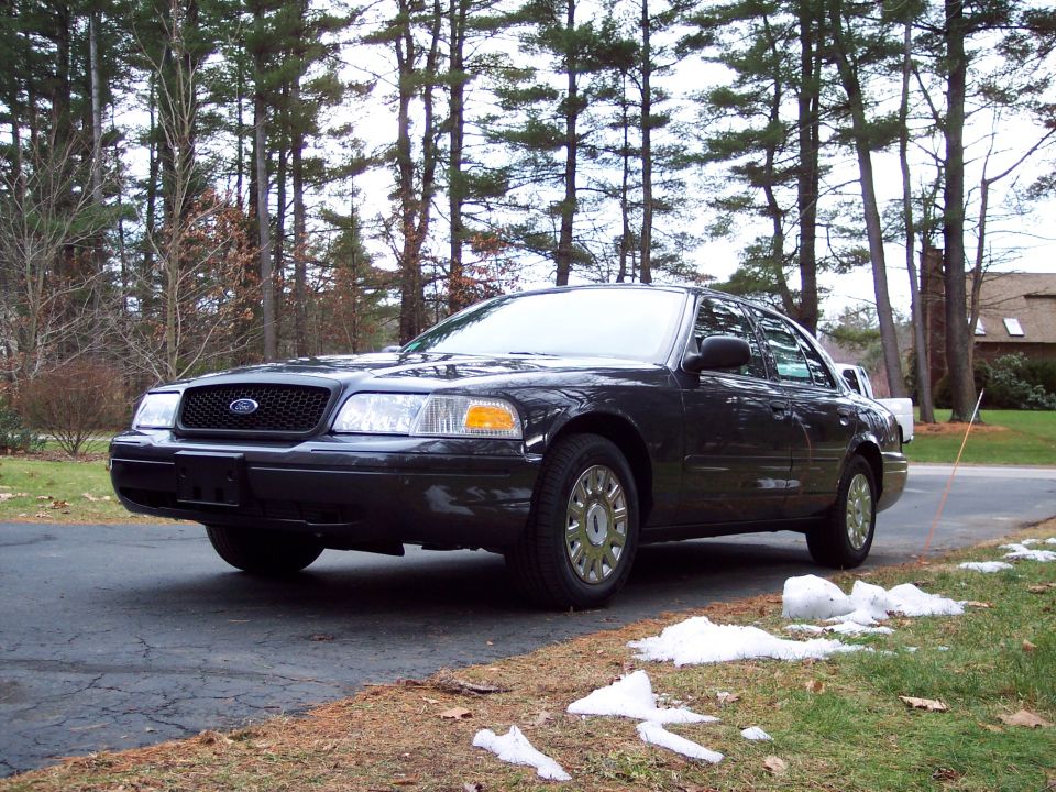 Dark-colored Ford Crown Victoria parked on a paved surface with trees in the background