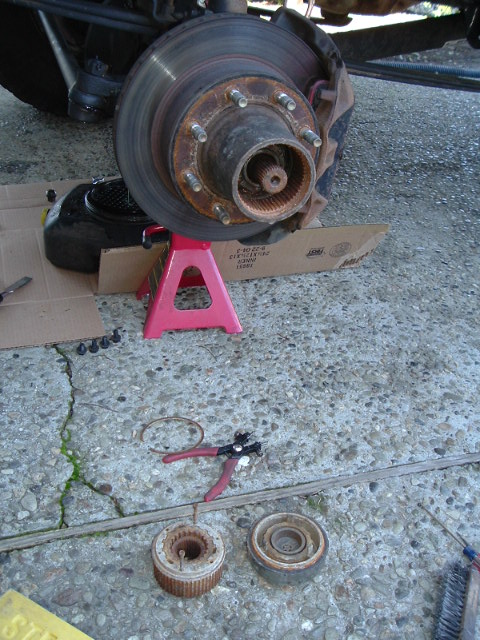 1989 Ford Bronco - Vehicle brake rotor and hub assembly on a jack stand with tools and parts laid out on the concrete.