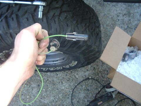 1989 Ford Bronco - Close-up of a hand holding electrical wiring and a connector, with a tire and a box in the background.