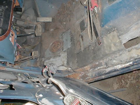 1987 Ford Bronco - The interior floor of a vehicle shows extensive rust damage and recent patch welding repairs.