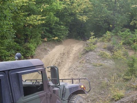 1996 Ford Bronco - A Humvee navigates a steep dirt path surrounded by trees, with another vehicle visible ahead.