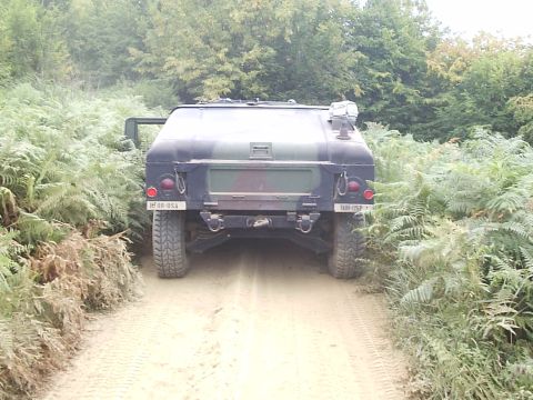 1996 Ford Bronco - A camouflaged military vehicle navigates a dirt track surrounded by dense foliage.