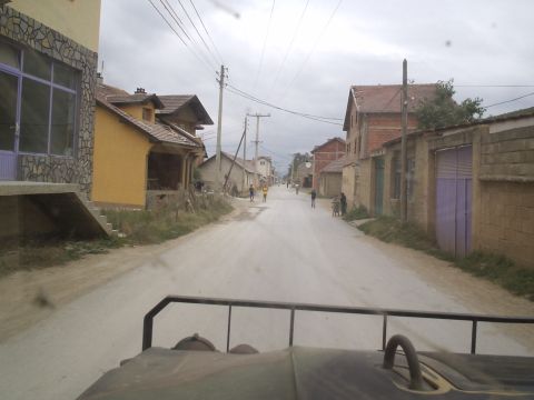 1996 Ford Bronco - A view down a dusty village road, with houses lining both sides and a few people walking.