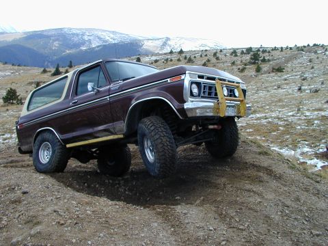 1979 Ford Bronco - A brown 1978 Ford Bronco with a white top and yellow brush guard navigates a dirt hill.