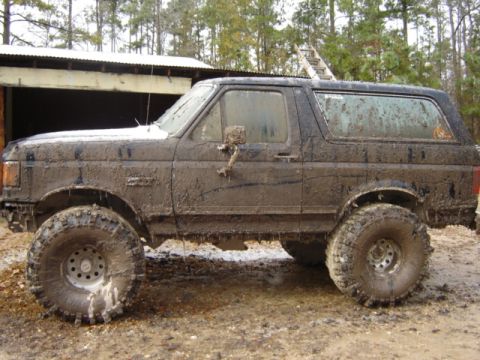 1989 Ford Bronco - Muddy 1989 Ford Bronco sits off-road, showing its lifted suspension and large tires.