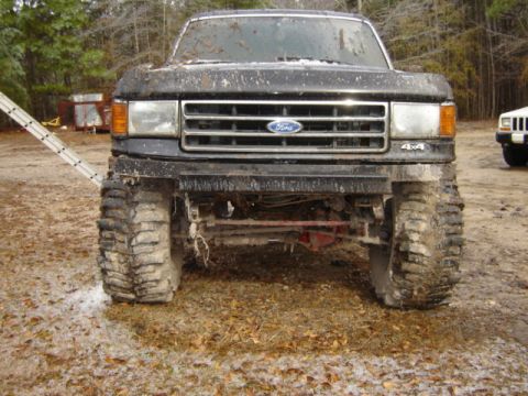 1989 Ford Bronco - This lifted Ford truck, likely from the late 1980s, is covered in mud. Another vehicle is partially visible in the background.