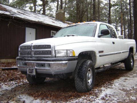 1989 Ford Bronco - A white Dodge Ram pickup truck is covered in ice and icicles, parked outside a rustic cabin in winter.