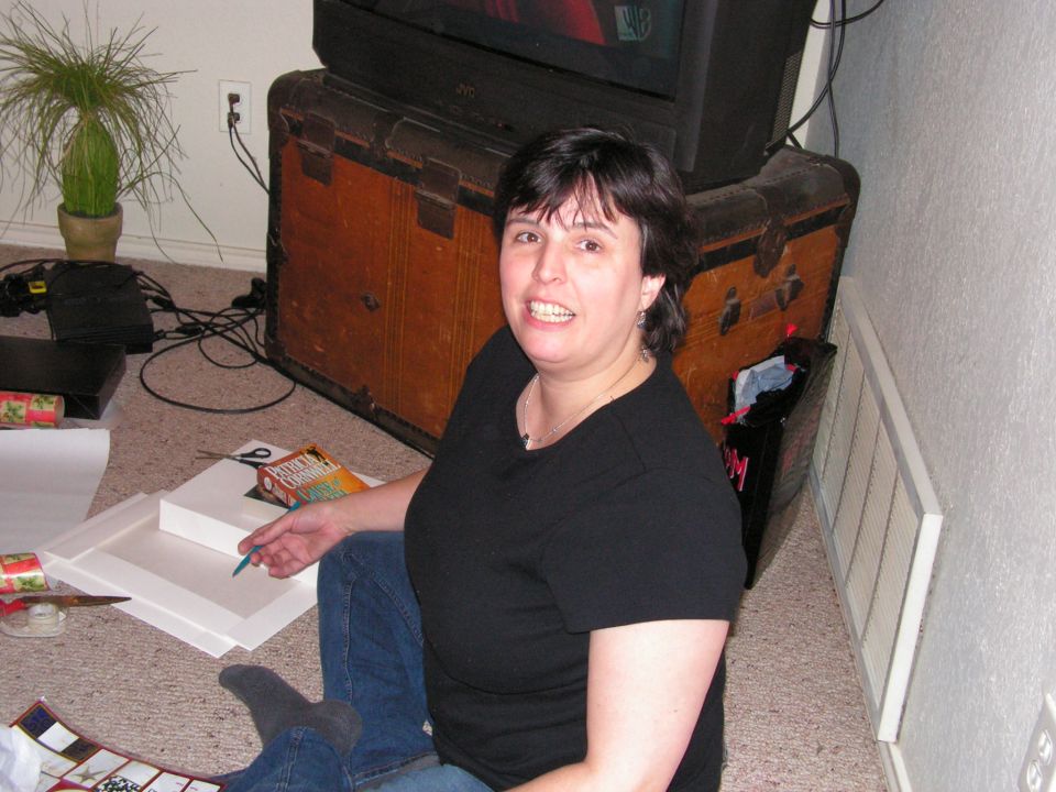 Smiling woman in black top sitting on floor by an old steamer trunk and TV