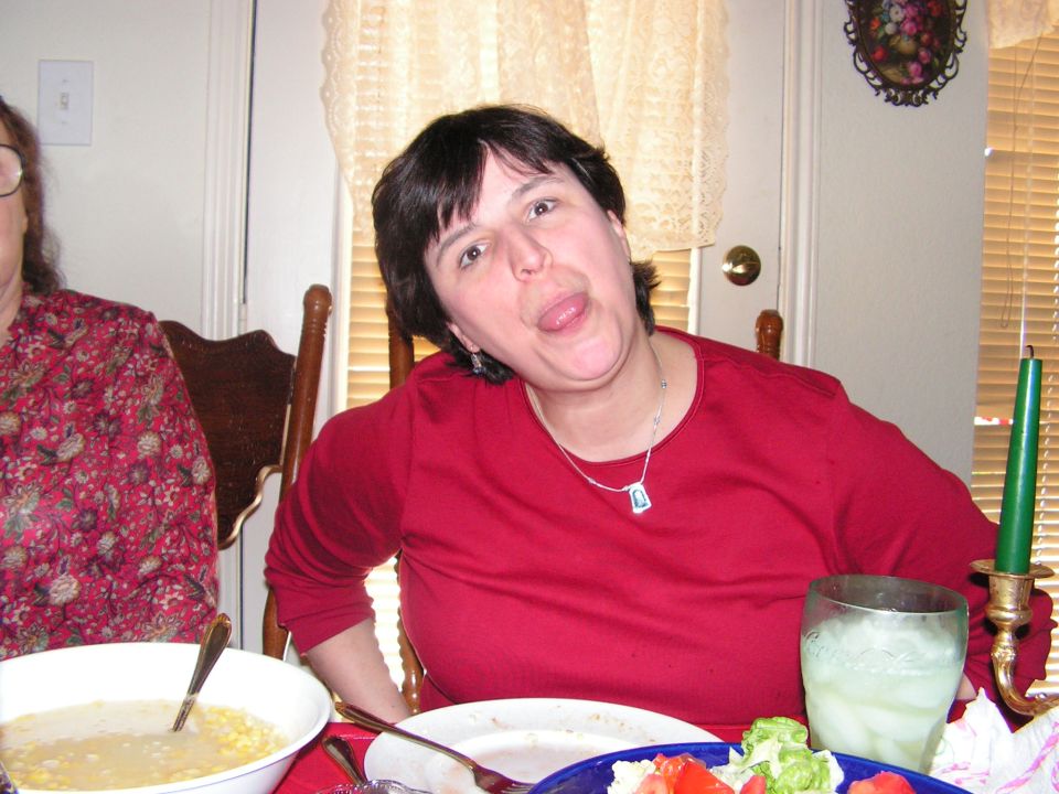 Woman sticking her tongue out at the camera, sitting at a table with food