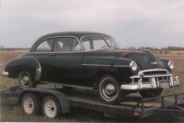 Black 1950s Chevrolet fastback two-door sedan loaded on a flatbed trailer in a field