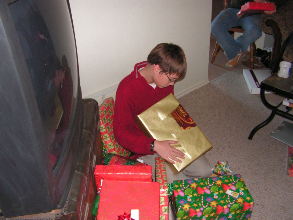 boy in red sweater opening a gold gift box, surrounded by other wrapped presents
