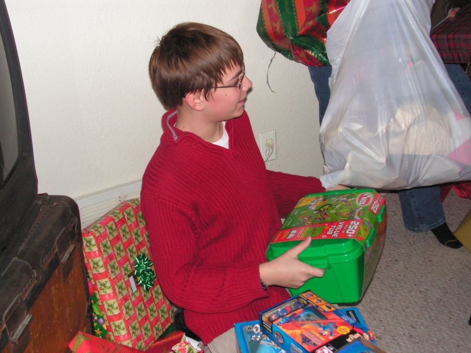 Kid in red sweater holding a green toy box, surrounded by wrapped presents