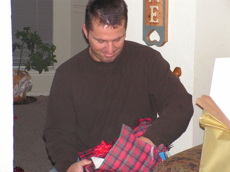 Man in brown shirt opening a red plaid gift with a red bow