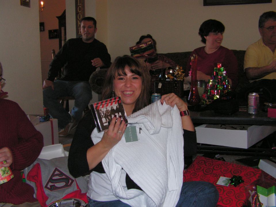 Woman holding a CD and white sweater, surrounded by gifts and people