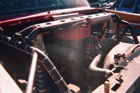 1990 Ford Bronco - Close-up of an off-road vehicle's engine bay showing a V8, red shock hoops, braided hoses and coil-over springs.