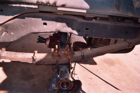 1990 Ford Bronco - Underside view of a vehicle's front axle showing leaf springs, a differential housing and an exposed wheel hub on dirt.