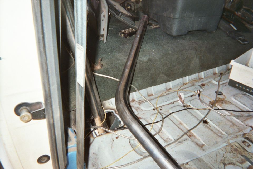 Interior corner of a stripped vehicle showing a bent tubular bar over bare carpet and floor