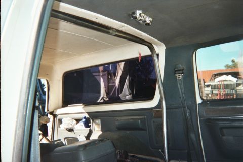 1990 Ford Bronco - Interior view of a vehicle's rear with the quarter window opening looking through the cabin to a parking lot outside.