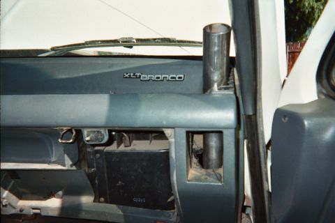 1990 Ford Bronco - gray dashboard bearing an XLT Bronco emblem, with a metal vent tube and exposed glovebox cavity on the passenger side.